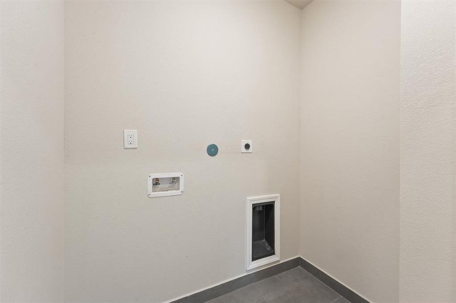 This is a compact utility space with neutral walls, tiled flooring, and is equipped with a pet door, electrical outlets, and wall hookups for appliances or electronics.