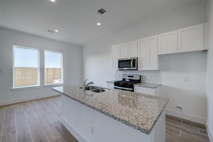 Alternate view of the space shows the kitchen and dining areas. Expansive granite countertops are complimented by chrome plumbing fixtures, whle oversized windows flood the room with natural light.