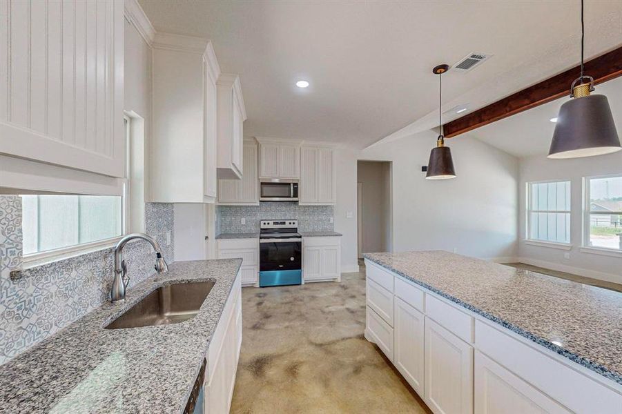 Kitchen featuring stainless steel appliances, hanging light fixtures, white cabinets, decorative backsplash, and sink