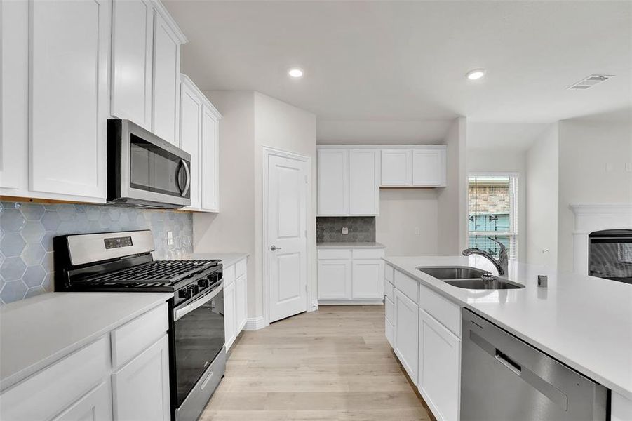 Kitchen with white cabinets, backsplash, light wood-type flooring, appliances with stainless steel finishes, and sink