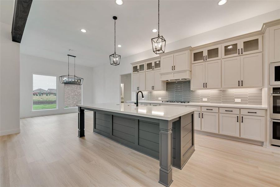 Kitchen featuring backsplash, light hardwood / wood-style flooring, pendant lighting, a kitchen island with sink, and cooktop