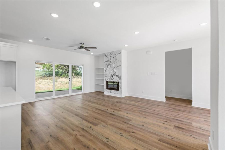 Unfurnished living room featuring a high end fireplace, ceiling fan, luxury vinyl flooring and built in features