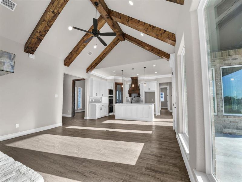 Unfurnished living room featuring beam ceiling, dark hardwood / wood-style floors, high vaulted ceiling, and ceiling fan