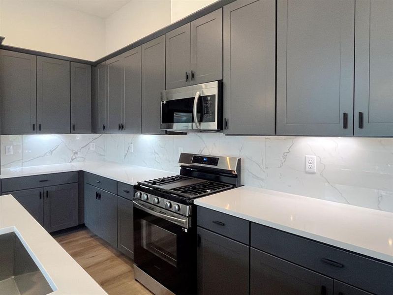 Modern Chef's Kitchen: Sleek gray cabinetry, premium stainless steel appliances, and elegant marble backsplash create a sophisticated space for culinary creativity.