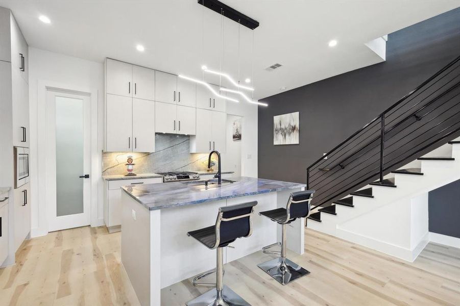 Kitchen featuring light hardwood / wood-style flooring, white cabinets, decorative backsplash, pendant lighting, and sink