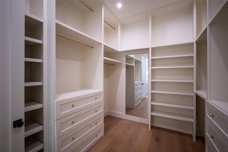 Primary closet with tons of shelving and built ins light hardwood / wood-style flooring