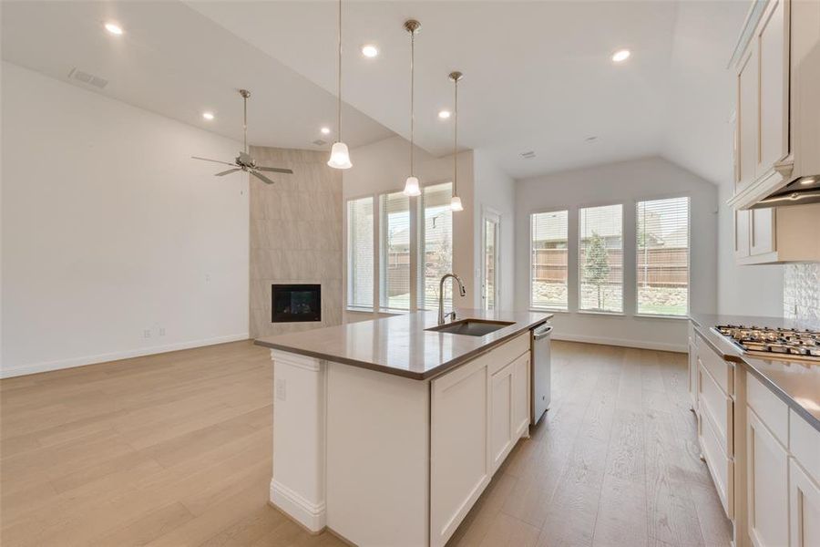 Kitchen featuring white cabinetry, light wood-type flooring, an island with sink, sink, and a tile fireplace