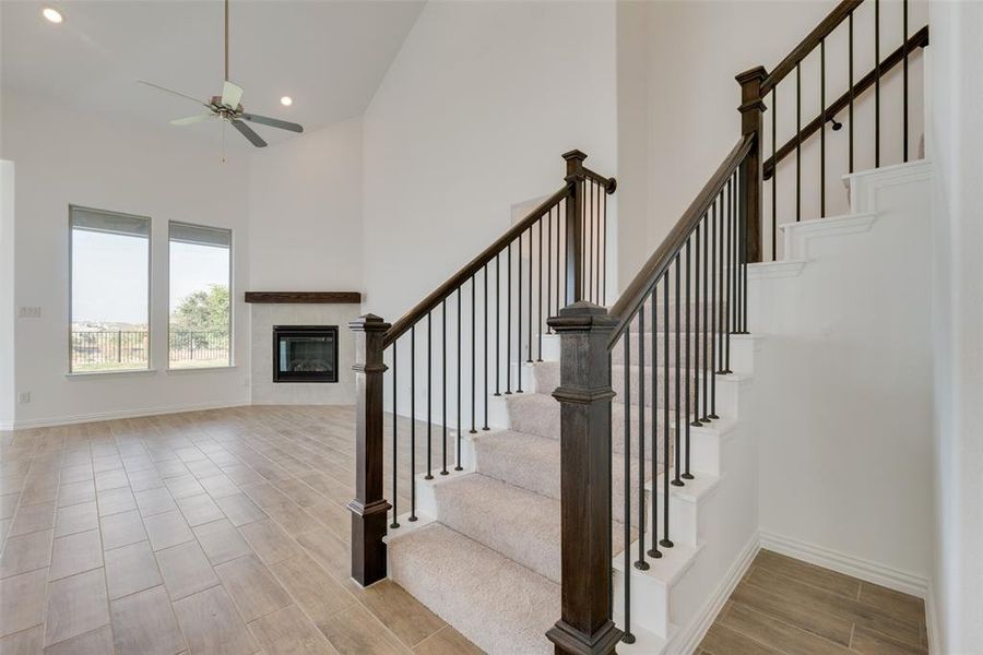 Staircase with a tiled fireplace, light hardwood / wood-style flooring, high vaulted ceiling, and ceiling fan