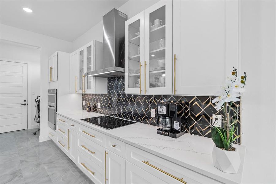 Kitchen featuring backsplash, wall chimney range hood, white cabinetry, black electric cooktop, and light stone countertops