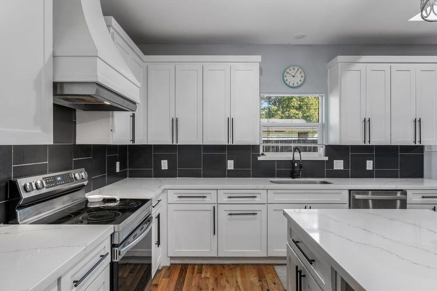 Kitchen featuring appliances with stainless steel finishes, white cabinetry, premium range hood, and sink