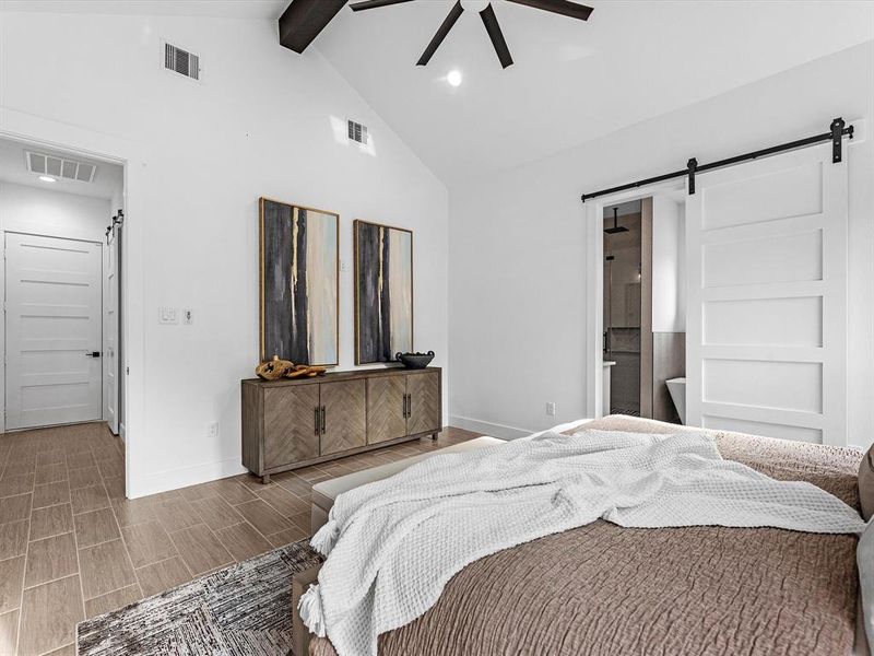 This spacious primary bedroom includes a 14-foot cathedral ceiling, an oversized black ceiling fan, and a modernized 5-panel barn door that separates it from the primary bathroom.