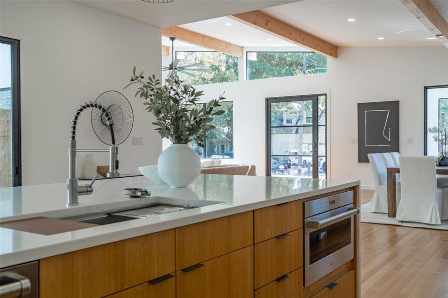 Kitchen with wolf appliances, vaulted ceiling with beams, sink, light hardwood / wood-style flooring, and oven