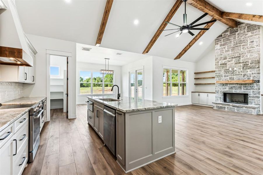 Kitchen featuring light wood-type flooring, premium range hood, stainless steel appliances, and a center island with sink