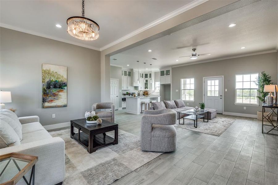 Living room with ceiling fan with notable chandelier, crown molding, and light wood-type flooring