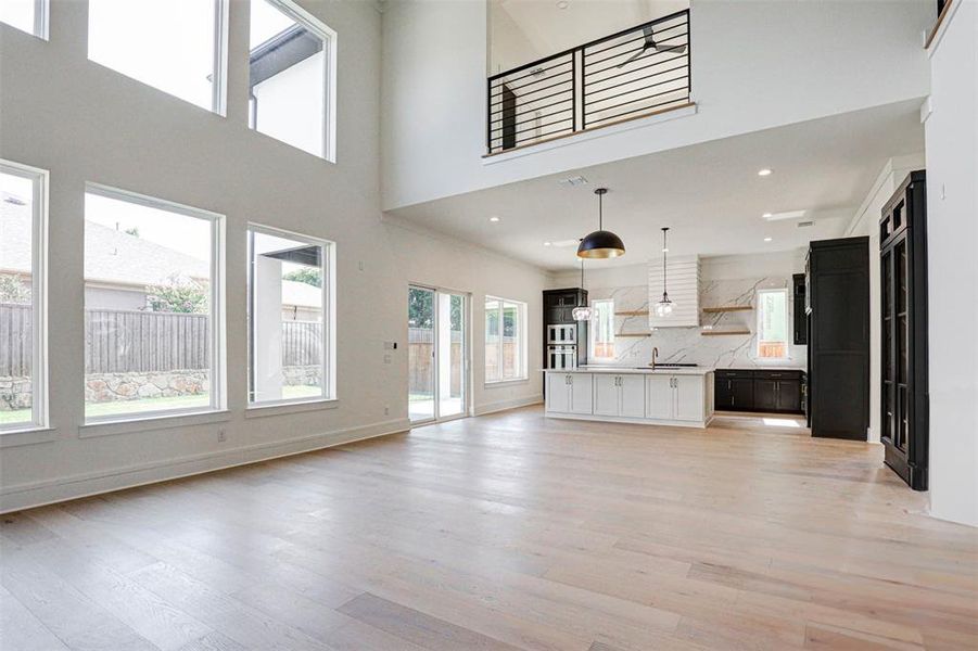 Unfurnished living room featuring a high ceiling, sink, and light hardwood / wood-style flooring