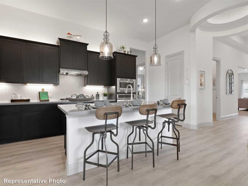 Kitchen featuring stainless steel appliances, a center island with sink, hanging light fixtures, decorative backsplash, and light wood-type flooring