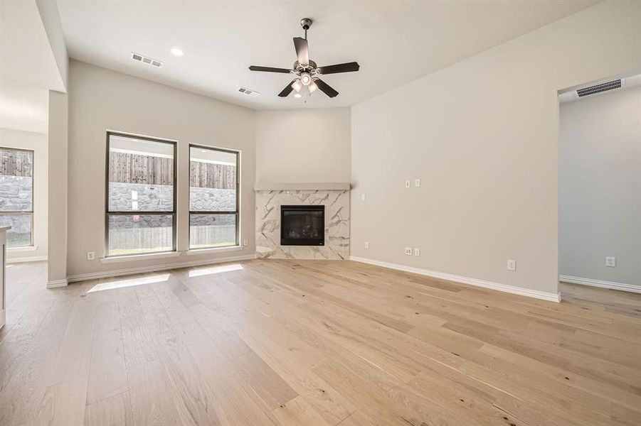 Unfurnished living room featuring a premium fireplace, light hardwood / wood-style floors, and ceiling fan