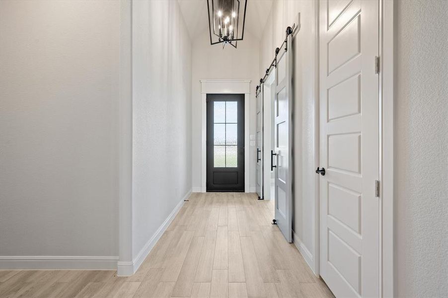 Corridor featuring a chandelier, light wood-type flooring, and a barn door