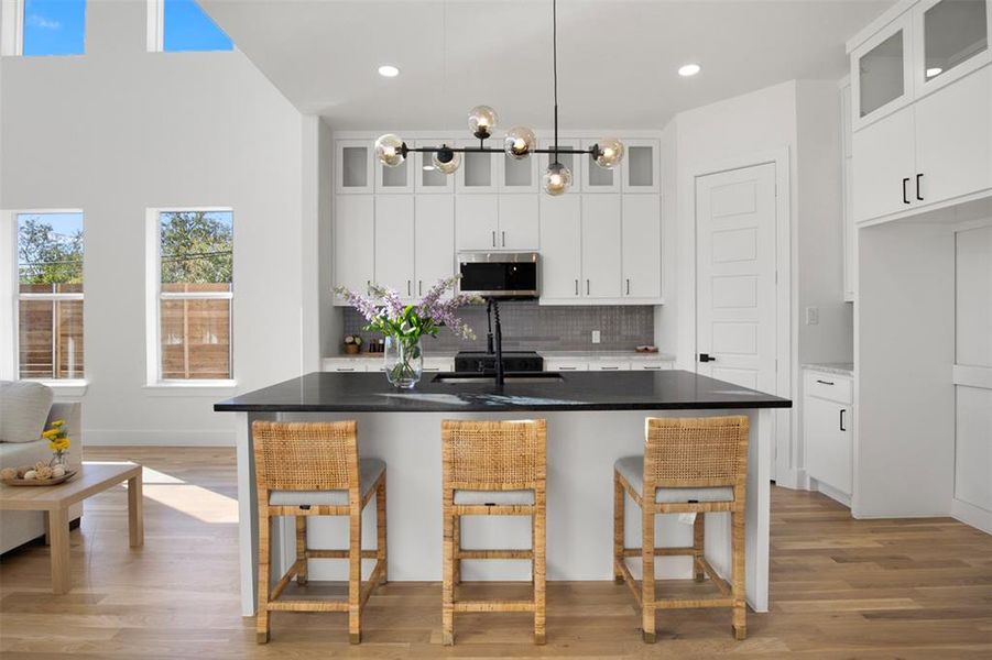 Kitchen featuring a kitchen breakfast bar, light hardwood / wood-style flooring, an island with sink, a chandelier, and white cabinets