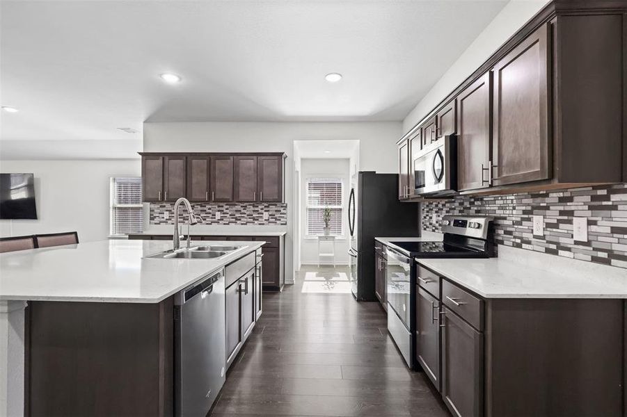 Kitchen with sink, dark hardwood / wood-style floors, an island with sink, appliances with stainless steel finishes, and dark brown cabinetry