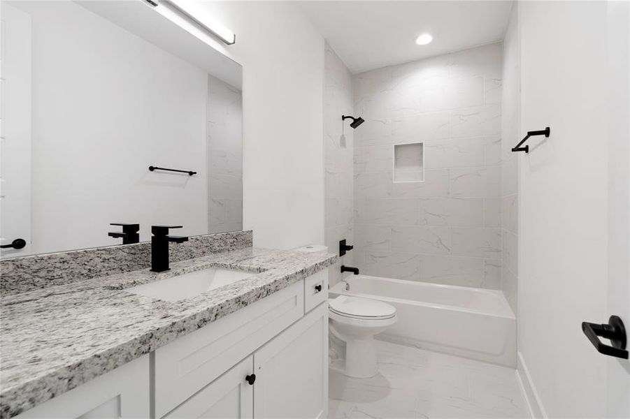 The secondary bathroom features sleek black accents and elegant ceramic tiles that extend from tub to ceiling, complete with a convenient shower niche