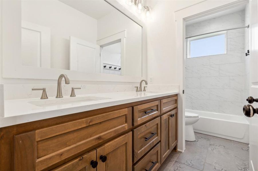Full bathroom featuring dual vanity, tiled shower / bath, tile floors, and toilet