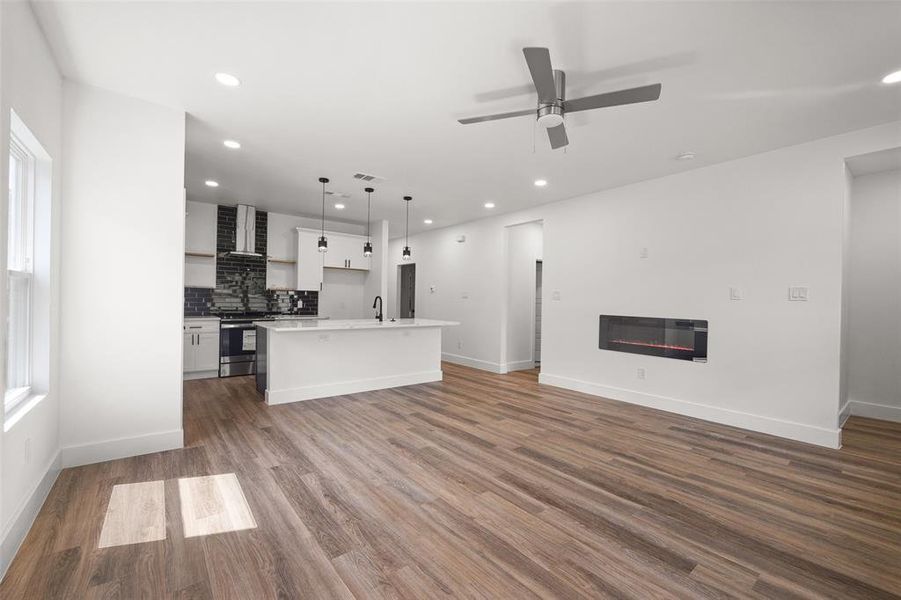 Kitchen with wall chimney range hood, white cabinets, tasteful backsplash, and wood-type flooring