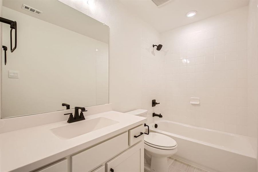 Full bathroom featuring vanity, tiled shower / bath combo, toilet, and tile patterned flooring