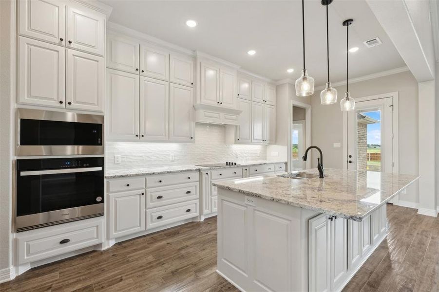 Kitchen with white cabinetry, an island with sink, crown molding, hardwood / wood-style flooring, and sink