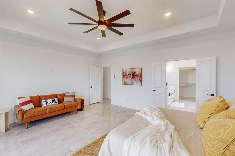 Tiled bedroom featuring a closet, a spacious closet, a high ceiling, a tray ceiling, and ceiling fan