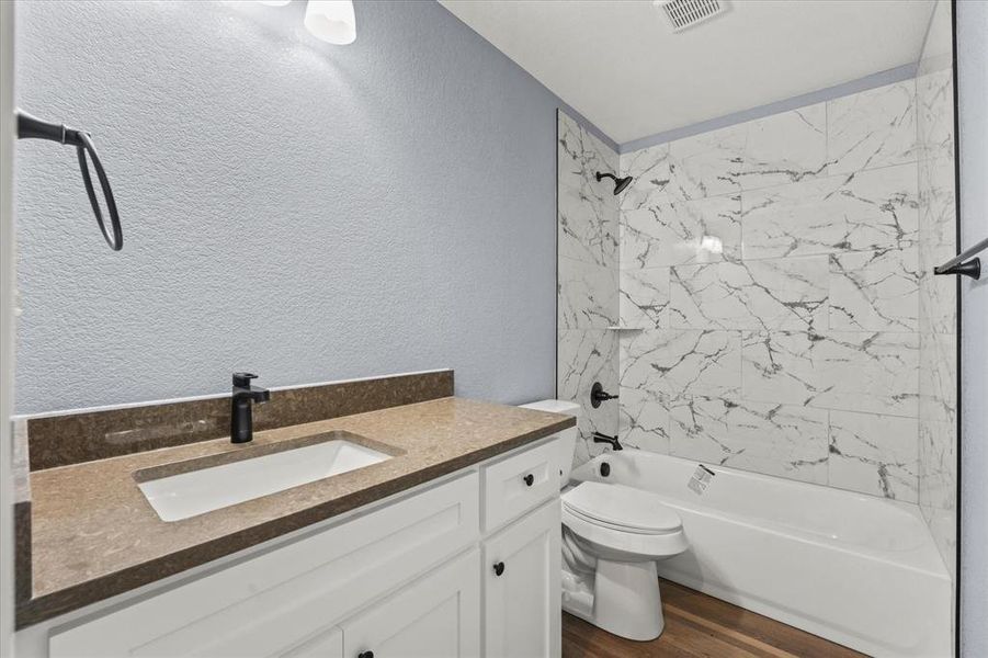 Full bathroom featuring toilet, vanity, tiled shower / bath, and hardwood / wood-style floors