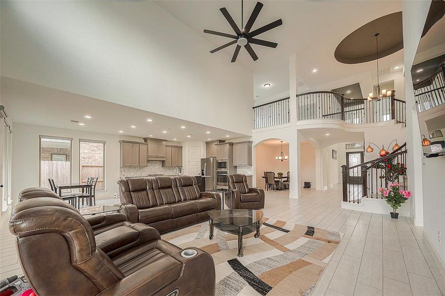 This is a spacious, open-concept living area with high ceilings, a modern kitchen, ample natural light, and a view of the upstairs balcony. It features comfortable seating, a dining area, and elegant tile flooring.
