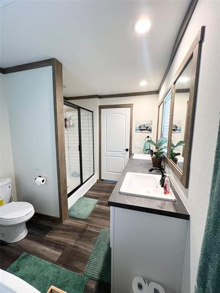 Bathroom featuring toilet, hardwood / wood-style floors, crown molding, vanity, and an enclosed shower