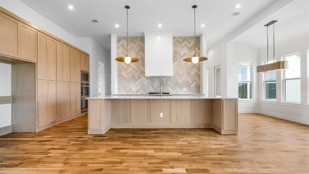 Kitchen featuring a center island with sink, pendant lighting, light brown cabinetry, and light hardwood / wood-style flooring