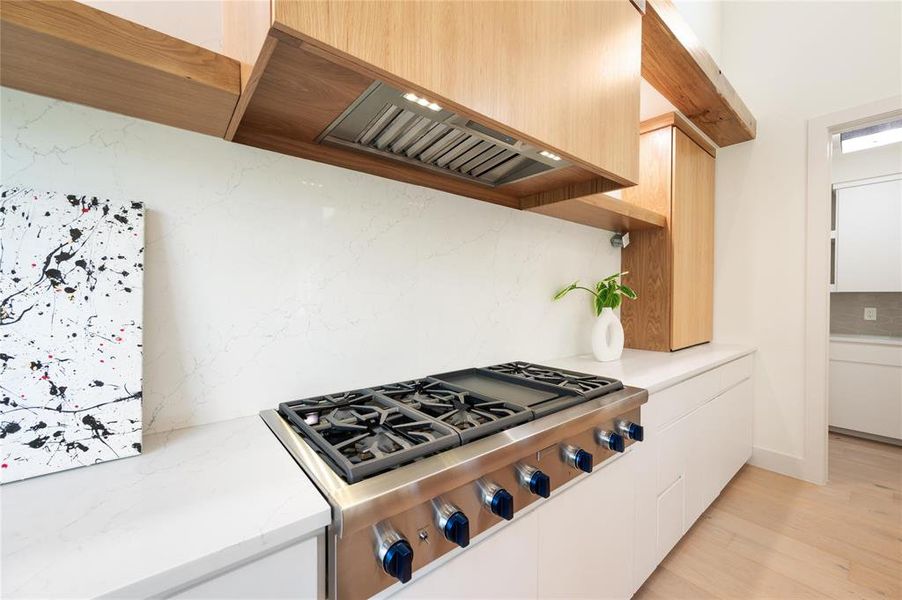 Kitchen featuring stove, light hardwood / wood-style floors, custom exhaust hood, light brown cabinetry, and white cabinetry