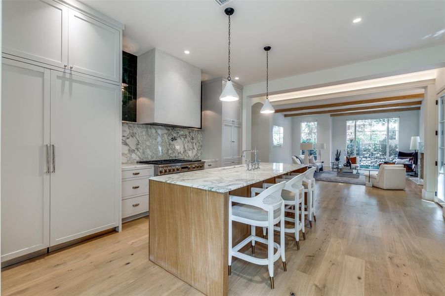 Kitchen with light wood-type flooring, pendant lighting, a kitchen breakfast bar, light stone counters, and an island with sink