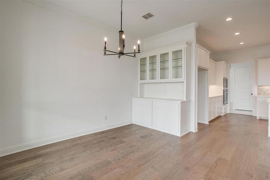 Unfurnished dining area with ornamental molding, an inviting chandelier, and light hardwood / wood-style floors