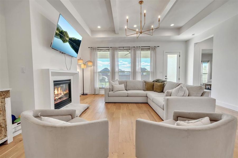 Living room featuring beamed ceiling, light hardwood / wood-style flooring, and a notable chandelier