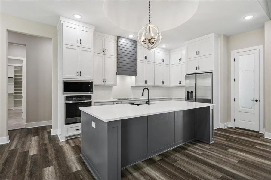 Kitchen with white cabinets, a center island with sink, dark wood-type flooring, and appliances with stainless steel finishes