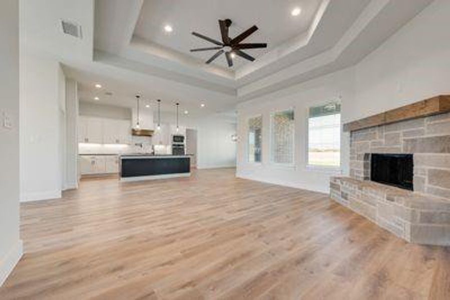 Unfurnished living room featuring a stone fireplace, light hardwood / wood-style flooring, a tray ceiling, and ceiling fan