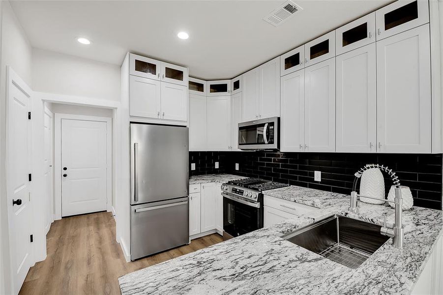 Kitchen featuring appliances with stainless steel finishes, light granite counters, light hardwood / wood-style floors, and white cabinets