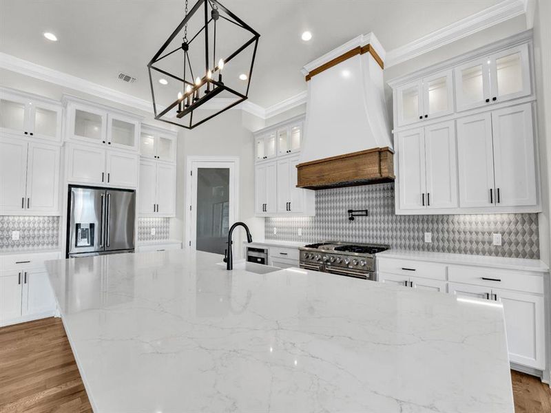 Kitchen with custom range hood, stainless steel appliances, sink, white cabinets, and light stone counters