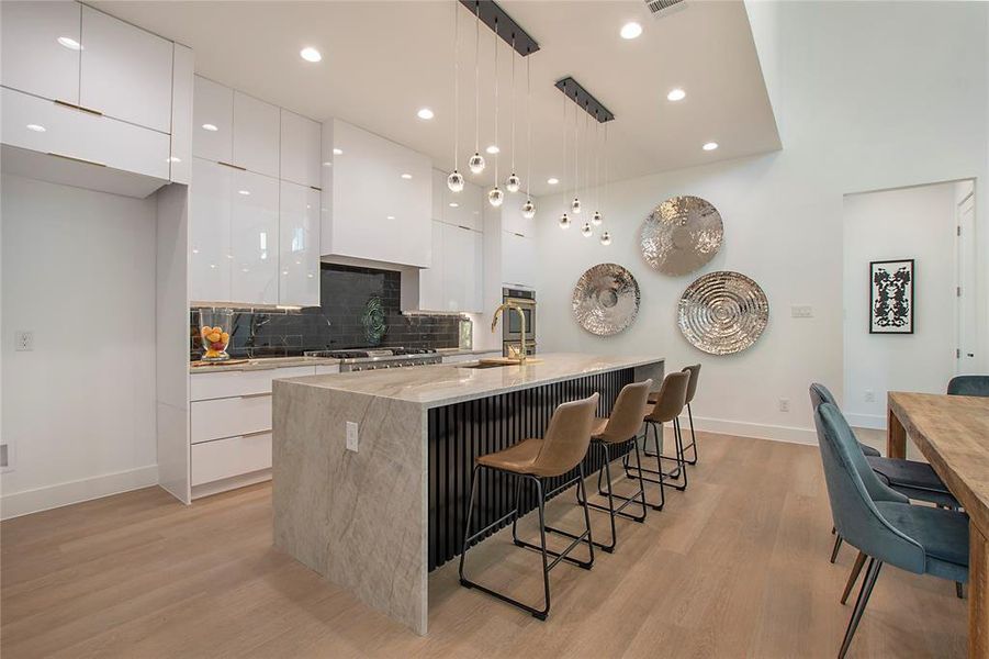 Kitchen featuring decorative backsplash, white cabinets, pendant lighting, light wood-type flooring, and a center island with sink