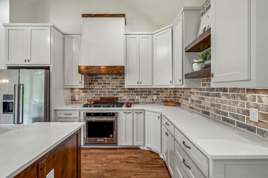 Kitchen with appliances with stainless steel finishes, light stone counters, wood-type flooring, and backsplash