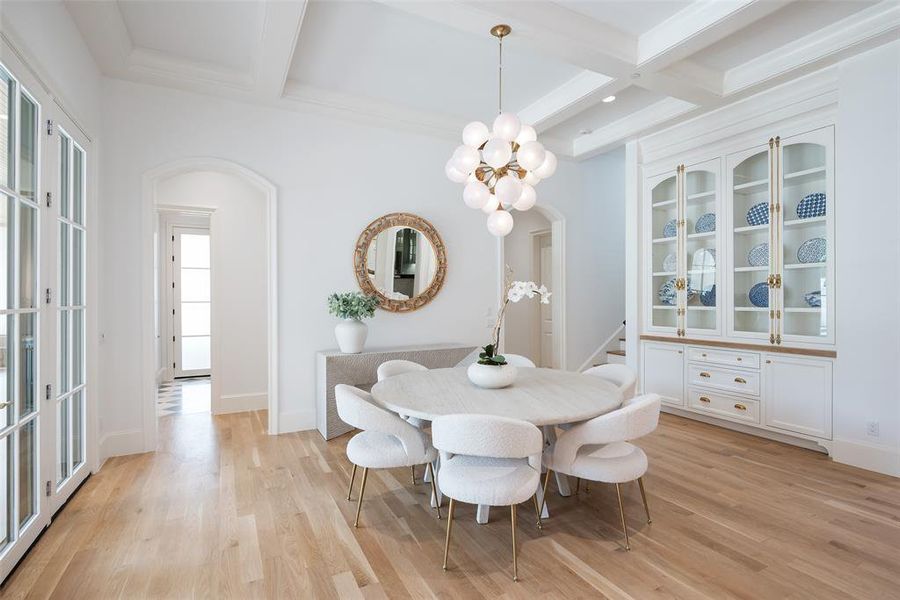 Dining space with light wood flooring, beamed ceiling, ornamental molding, coffered ceiling, and french doors