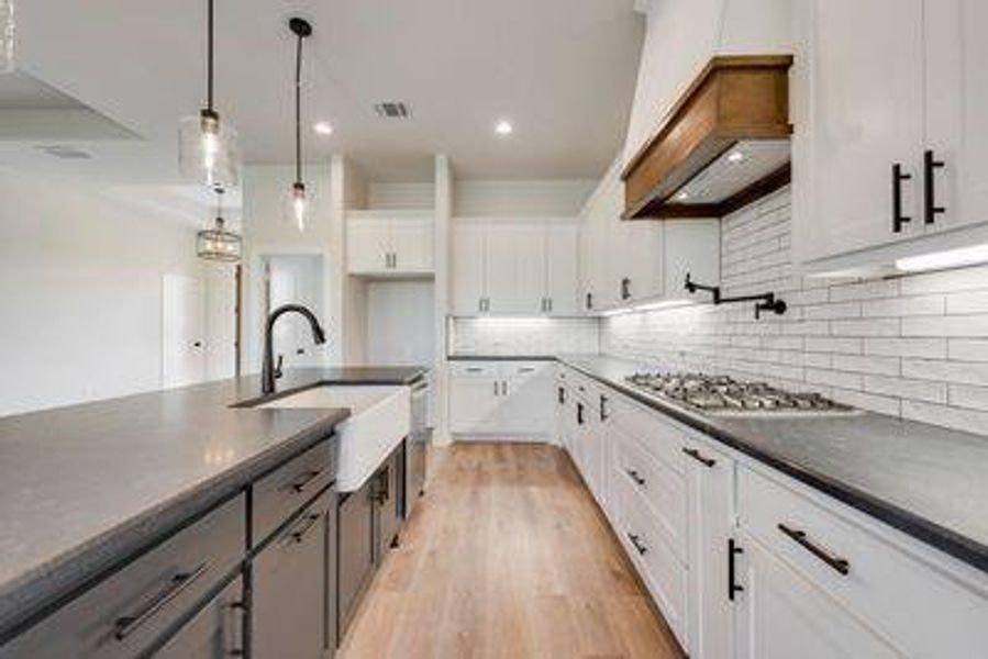 Kitchen featuring custom exhaust hood, white cabinetry, light hardwood / wood-style flooring, stainless steel gas cooktop, and decorative light fixtures