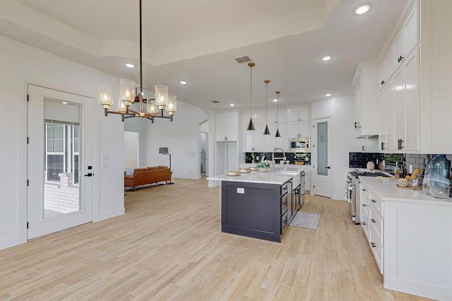 Kitchen with white cabinetry, light wood-type flooring, a raised ceiling, a center island with sink, and appliances with stainless steel finishes