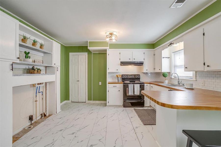 Kitchen with sink, kitchen peninsula, white cabinets, black / electric stove, and decorative backsplash