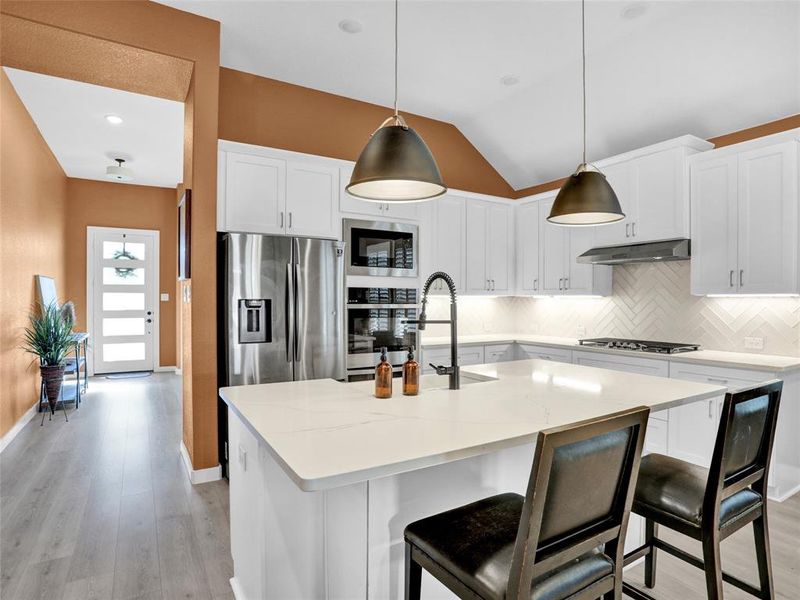 Gorgeous modern kitchen with double ovens, quartz counters, farmhouse sink, island and gas stovetop.