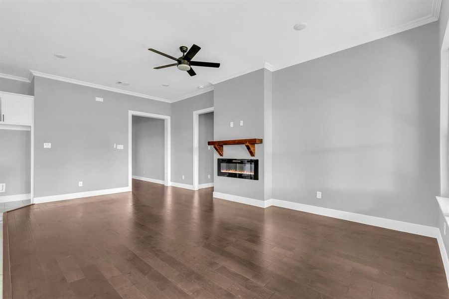 Unfurnished living room featuring ceiling fan, ornamental molding, and dark hardwood / wood-style flooring